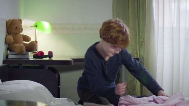 Cute Caucasian redhead boy trying on pink shirt. Smiling child getting dressed in his bedroom at home. Portrait, fashion, childhood. - Footage, Video
