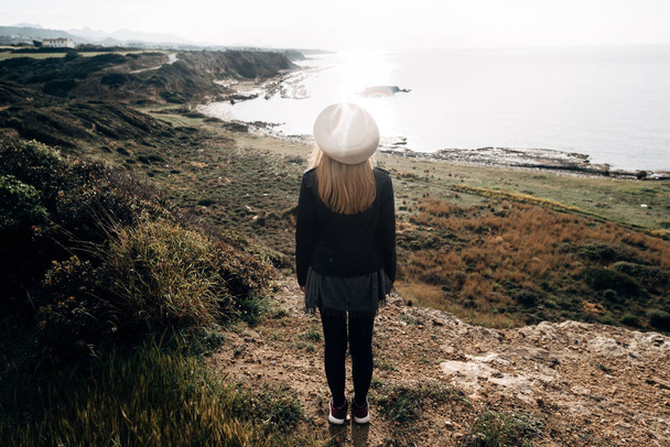 A girl in a hat stands and looks at the sea - Фото, изображение