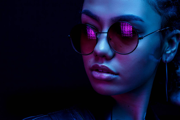 portrait of an African American young woman in sunglasses isolated on a black background in neon light - Zdjęcie, obraz
