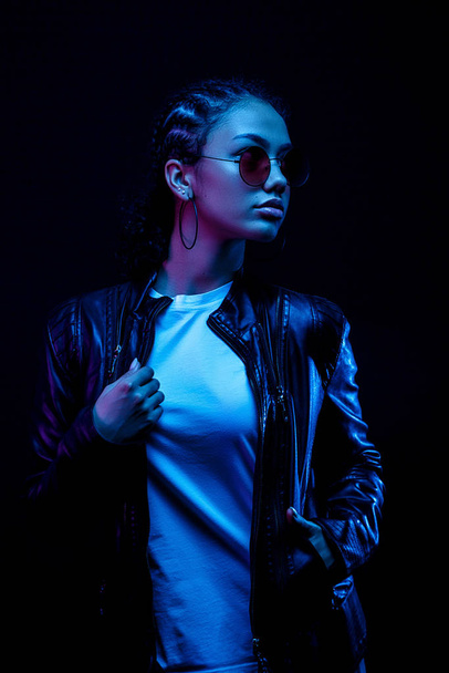 portrait of an African American young woman in sunglasses isolated on a black background in neon light - 写真・画像