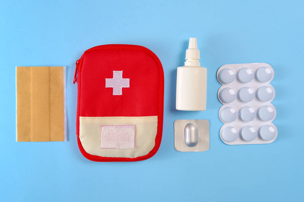 Closed tourist first aid kit pouch near to the pills, adhesive bandages and nasal spray on the bright blue background - Фото, зображення