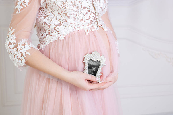 Egy terhes nő, aki ultrahangot tart a hasán. A terhes nő élvezi az első képet a meg nem született babájáról, előre megjósolva a jövőbeli élet másolási helyét. Egészséges terhességi koncepció - Fotó, kép