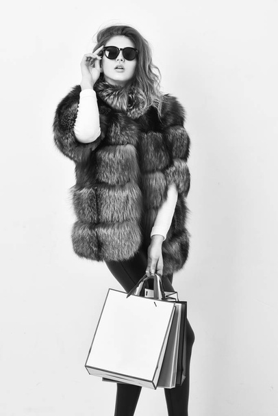 Buy with discount on black friday. Shopping or birthday gift. Woman shopping luxury boutique. Girl wear sunglasses and furry coat shopping white background. Lady hold shopping bags. Discount and sale - Foto, imagen