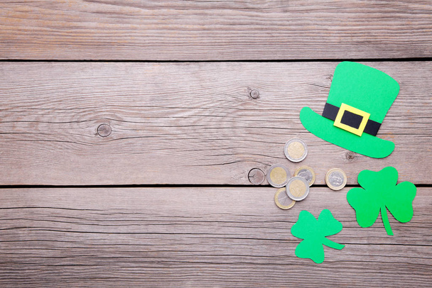 Happy Saint Patrick's of handmade paper clover leaves and hat with coins on grey wooden background. - Photo, image