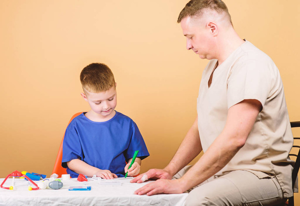 Boy cute child and his father doctor. Hospital worker. First aid. Medical help. Trauma and injurie. Medicine concept. Kid little doctor sit table medical tools. Health care. Medical examination - Фото, зображення