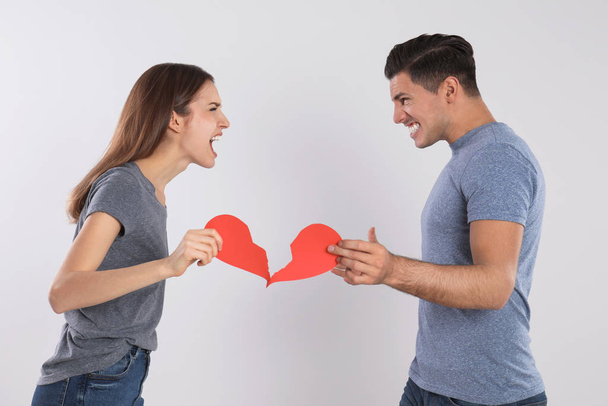 Couple with torn paper heart quarreling on light background. Relationship problems - Foto, Imagen