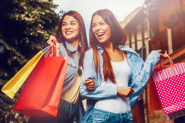 Alışveriş çılgınlığı! İki genç kadın alışveriş yaptıktan sonra mutlu olurlar. Gülümsüyor ve sokakta yürüyordu. - Fotoğraf, Görsel