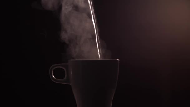 Hot boiled water is poured into a white ceramic cup or mug on black background with light - Video, Çekim