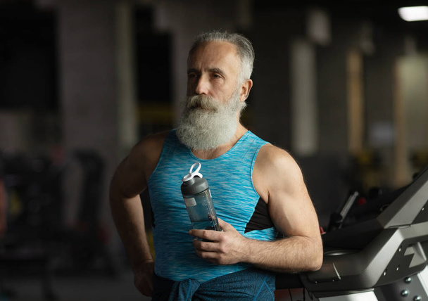 Idős szakállas férfi egy edzőteremben. Pihenés edzés után - Fotó, kép