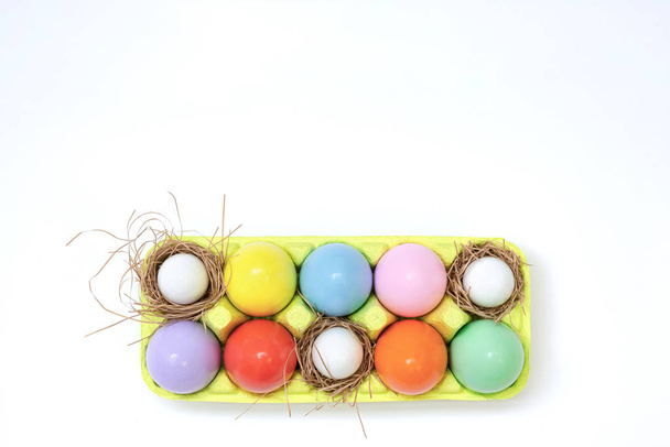 Widok z góry Kompozycja wielkanocna malowanych jaj w jaskrawych soczystych kolorach o błyszczącej fakturze, które leżą w pojemniku z gniazdami siana. Koncepcja wakacji, płaski układ, Wielkanoc, tło. - Zdjęcie, obraz