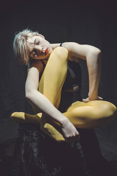 Hermosa chica sentada sobre fondo negro en pantimedias amarillas
 - Foto, Imagen