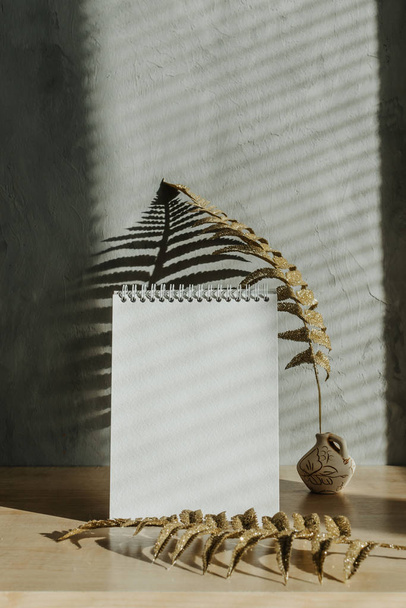 Modern trend home decor mockup with shadows and golden leaves. Fall autumn minimal mock up with open empty note pad, golden fern leaves and candle on grey concrete wall background. - Foto, imagen