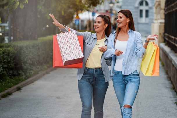 Alışveriş çılgınlığı! İki genç kadın alışveriş yaptıktan sonra mutlu olurlar. Gülümsüyor ve sokakta yürüyordu. - Fotoğraf, Görsel