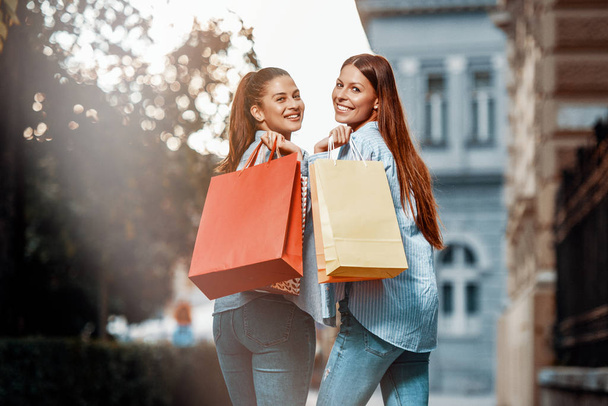 Kaufwahn! Zwei junge Frauen freuen sich nach dem Einkaufen. lächelnd die Straße hinunter - Foto, Bild