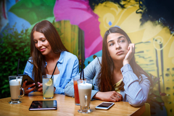 Twee vriendinnen in de cofee bar. Een van hen is boos omdat haar vriendin chatten aan de telefoon belangrijker vindt.  - Foto, afbeelding