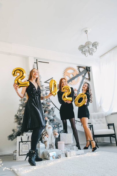 Silvesterparty 2020. schöne Frauen feiern Neujahr 2020. drei glückliche Mädchen in schwarzen metallischen Partykleidern mit goldenen Luftballons 2020 - Foto, Bild