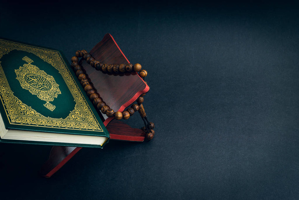 Αγία Al Quran με γραπτή αραβική καλλιγραφία έννοια του Al Quran και tasbih ή κομπολόι χάντρες σε μαύρο φόντο. Επιλεκτική εστίαση και τμήμα καλλιέργειας - Φωτογραφία, εικόνα