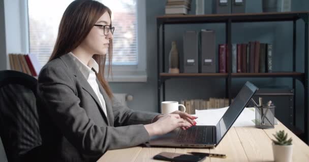 Zijaanzicht van serieuze dame die werkt op laptop op modern kantoor - Video