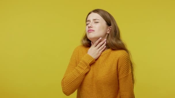 Flu symptoms and epidemic. Sick girl closing eyes in pain and touching painful neck, frowning suffering sore throat or tonsillitis, feeling unhealthy, hard to swallow. studio shot, yellow background - 映像、動画
