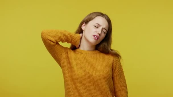 Sick unhappy girl closing eyes in pain and touching painful neck, frowning suffering from aching muscles, feeling unhealthy, hard to mp4e head. indoor studio shot isolated on yellow background - Video, Çekim