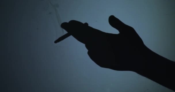 Czarna sylwetka dłoni, w której papieros na niebieskim tle - Materiał filmowy, wideo