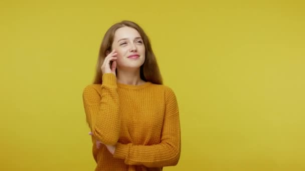 Beautiful lovely young woman with brown hair dreaming with peaceful expression, twisting curls on finger and having shy girlish fantasy, pleasant wish. studio shot isolated on yellow background - Filmagem, Vídeo