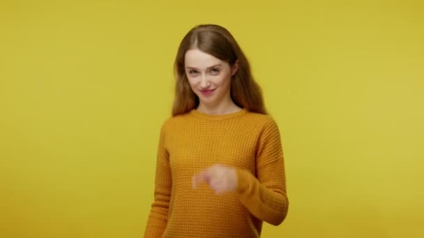Beautiful playful girl with brown hair pointing to camera and showing call me gesture with hand shaped like telephone, flirting, asking contact by phone. studio shot isolated on yellow background - Video