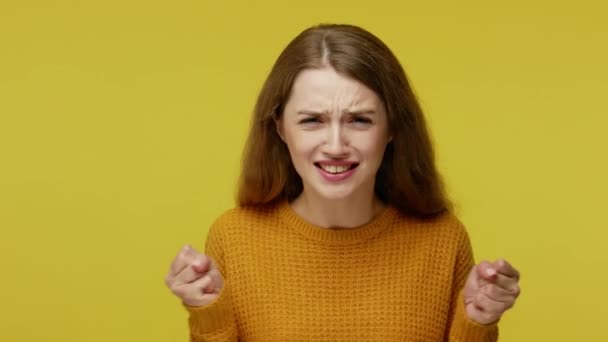 Temper and rage. Mad furious girl with brown hair in pullover expressing hate irritation, clenching her fists and screaming with anger to camera. indoor studio shot isolated on yellow background - Video
