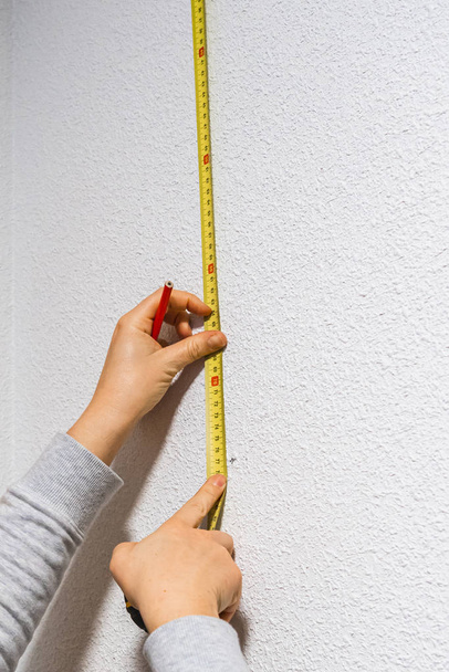 Женщина делает измерения на стене с помощью измерительной ленты
 - Фото, изображение