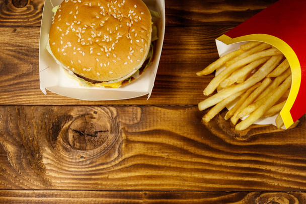 Big hamburger and french fries on wooden table - Фото, зображення