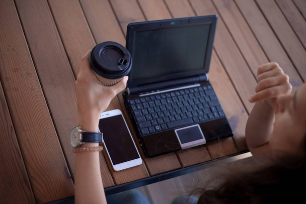 Jovens mãos femininas com uma manicura modesta, com grandes relógios de pulso, trabalham em um laptop, em pé em uma mesa de madeira
. - Foto, Imagem
