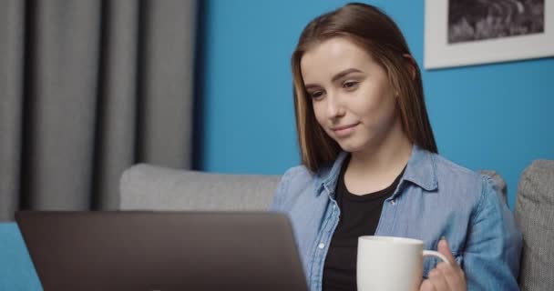 Smiling girl drinking coffee and using laptop at home - Filmagem, Vídeo