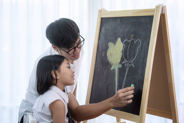 Ο Ασιάτης δάσκαλος μαθαίνει στους μαθητές να ζωγραφίζουν ένα λουλούδι σε ένα Μπλάκμπορντ. - Φωτογραφία, εικόνα
