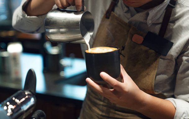 Closeup image of male barista holding and pouring milk for prepa - Photo, image