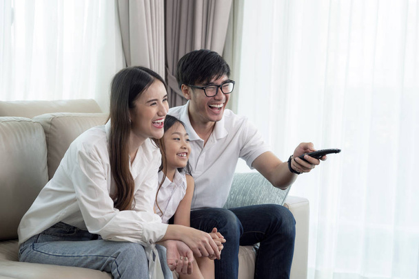 Aziatisch familie genieten van op zoek lcd tv op de bank in de woonkamer - Foto, afbeelding