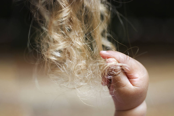 babyhand reaches into blonde curl - Фото, зображення