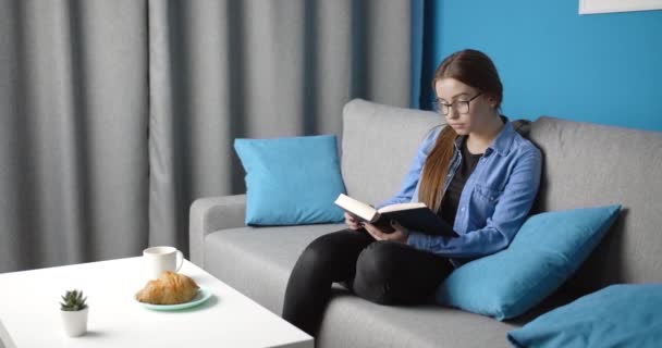 Bájos fiatal hölgy könyvet olvas kávéval otthon - Felvétel, videó