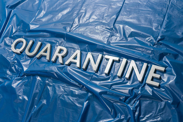 het woord quarantaine gelegd met zilveren letters op verfrommelde blauwe plastic folie in diagonaal perspectief - Foto, afbeelding