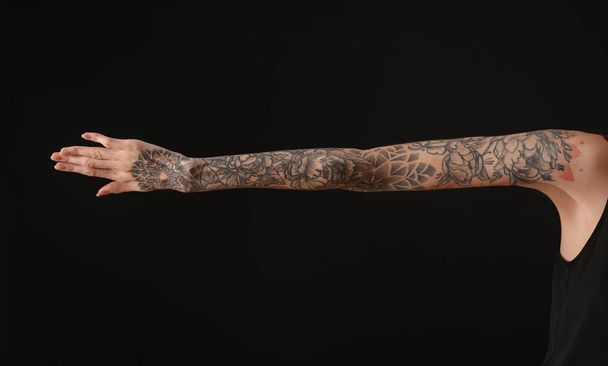 Woman with colorful tattoos on arm against black background, closeup - 写真・画像