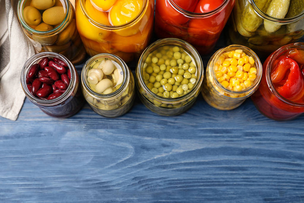 Glass jars with different pickled vegetables on blue wooden tabl - Фото, изображение