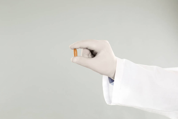 Doctor holding suppository for hemorrhoid treatment on light grey background, closeup - 写真・画像