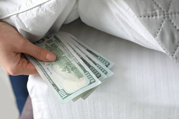 Woman hiding dollar banknotes under blanket in bedroom, closeup. Money savings - Foto, afbeelding