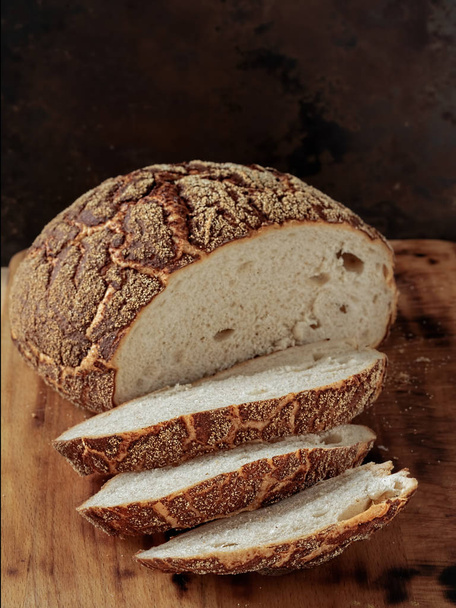 Čerstvě upečený chleba nakrájený na rustikální stůl. Detail, svislá orientace. - Fotografie, Obrázek