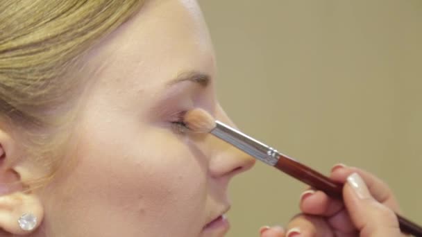 Professionele make-up kunstenaar met een borstel brengt oogschaduw aan op een klant in een schoonheidssalon. - Video