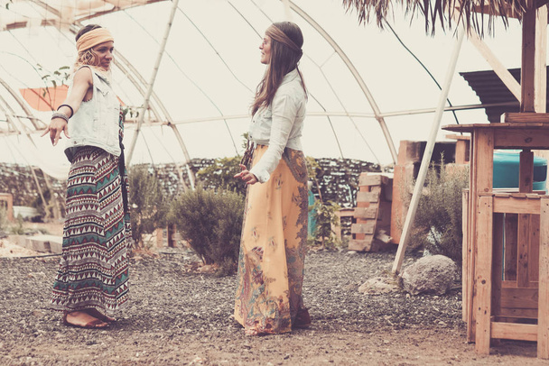 Хиппи и бесплатная альтернативная концепция образа жизни с парой молодых подруг, стоящих и говорящих на открытом воздухе в разноцветной одежде - Фото, изображение