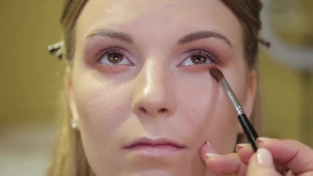 Professional make-up artist with a brush applies eye shadow to a client in a beauty salon. - Felvétel, videó