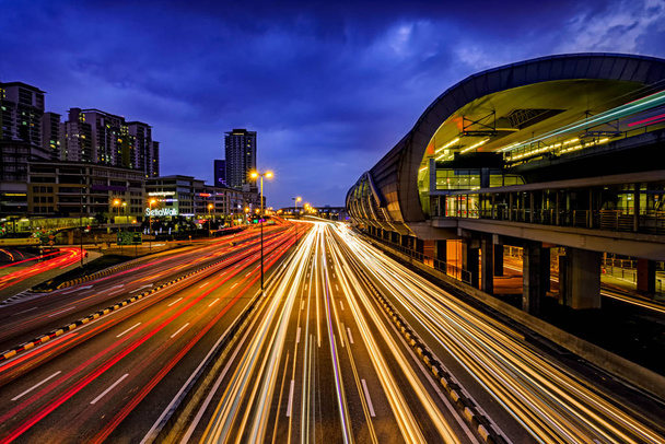 Sentier lumineux de trafic achalandé avec la gare ferroviaire LRT, les immeubles de bureaux et le ciel bleu foncé à l'arrière-plan à Puchong, Malaisie
. - Photo, image