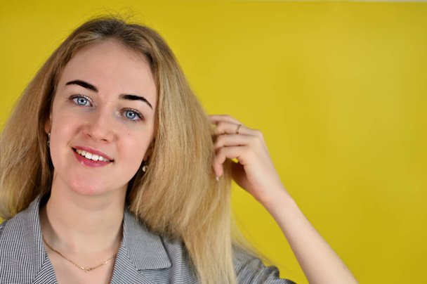 Nahaufnahme Porträt einer hübschen lächelnden jungen blonden Geschäftsfrau mit minimalem Make-up in einem grauen Anzug auf gelbem Hintergrund. er steht der Kamera in verschiedenen Posen direkt gegenüber. - Foto, Bild