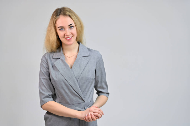 Model Standing directly in front of the camera in various poses. Portrait of a pretty cute smiling young blonde business woman with minimal makeup in a gray suit on a white background. - Фото, зображення