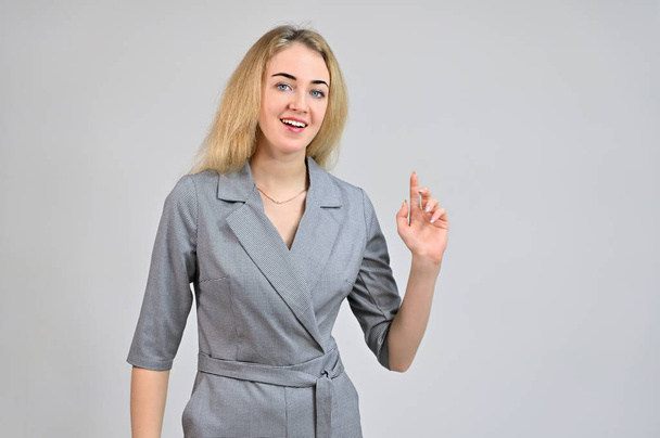 Model Standing directly in front of the camera in various poses. Portrait of a pretty cute smiling young blonde business woman with minimal makeup in a gray suit on a white background. - Valokuva, kuva